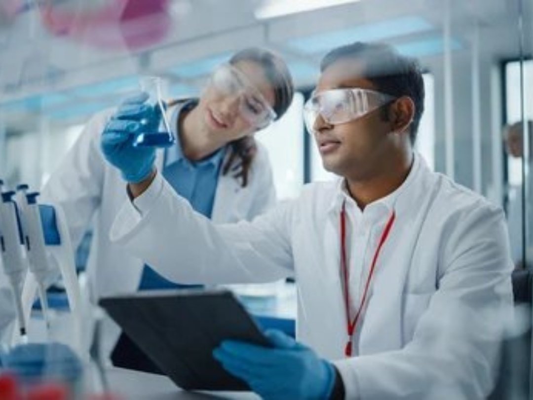 Two scientists in a lab coat examining a beaker, potentially involved in drug testing record keeping.