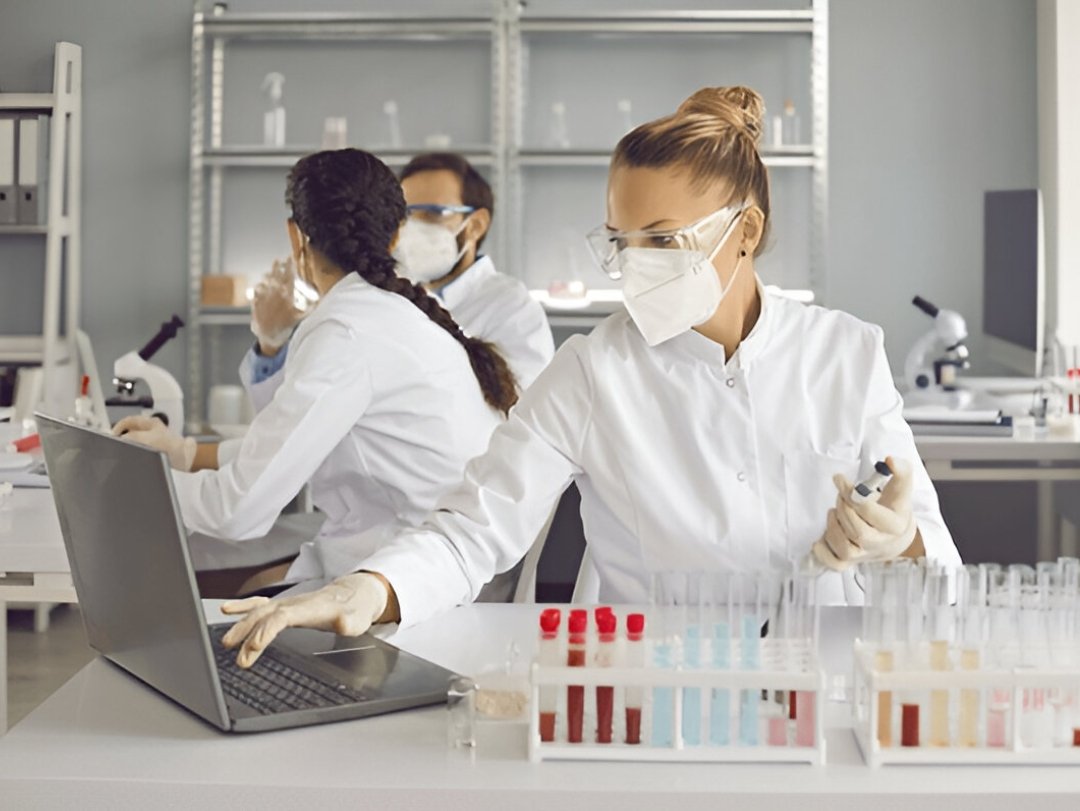 Lab workers in masks and gloves, possibly offering Drug Testing Service Customization, with laptops and test tubes.