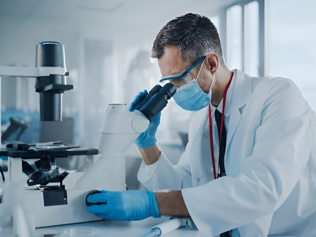 A scientist in protective gear using a microscope, representing drug testing technology in a lab.